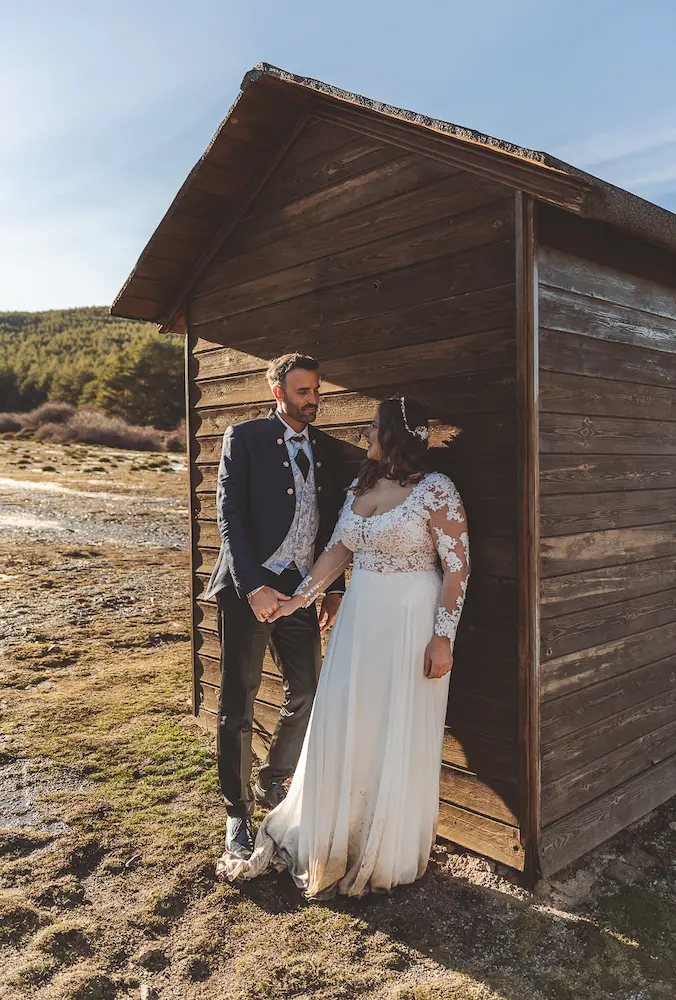 Pareja apoyada en una cabaña durante su postboda en la montaña